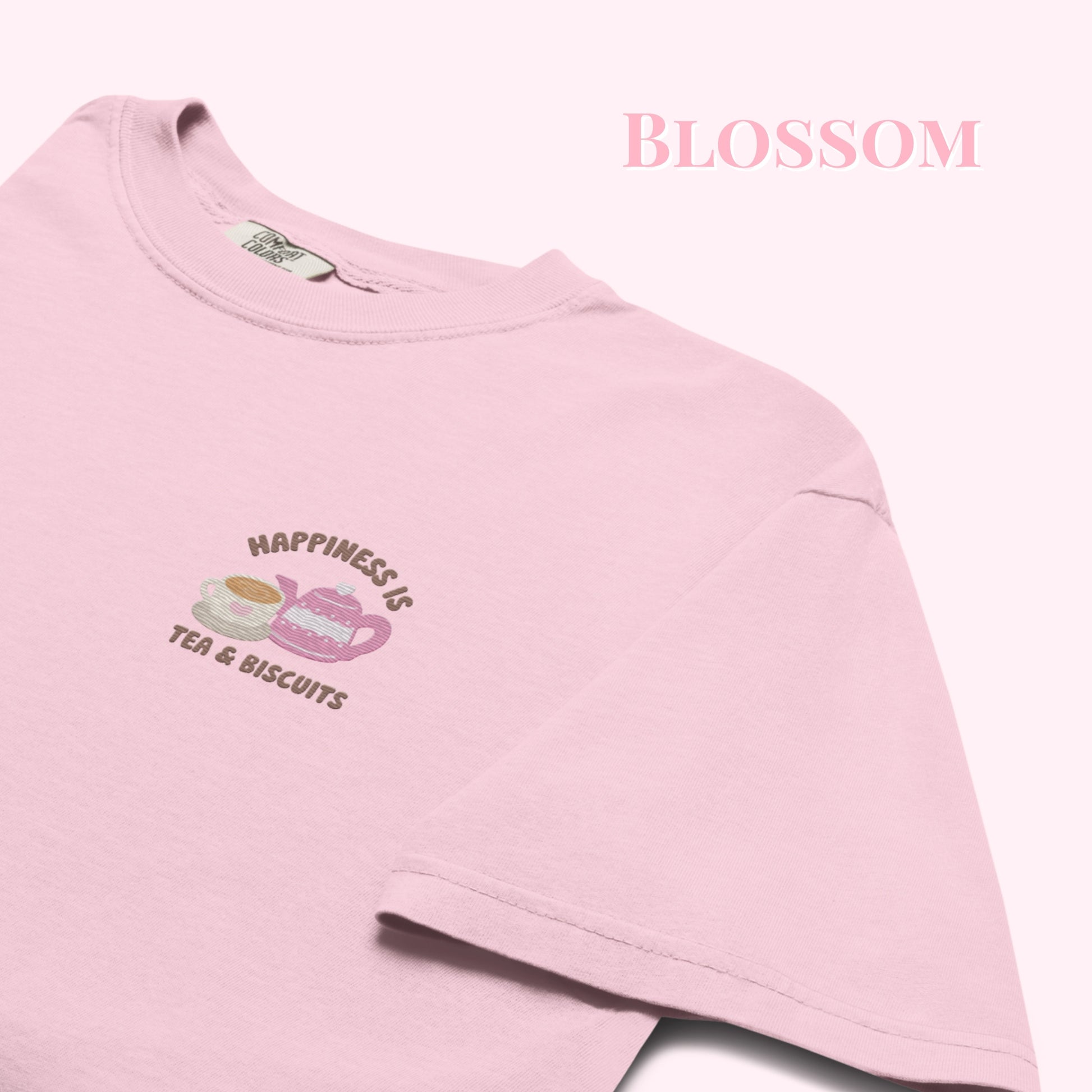 Close-up of "Happiness is Tea and Biscuits" script with a tiny embroidered teacup and teapot on a pink-coloured t-shirt