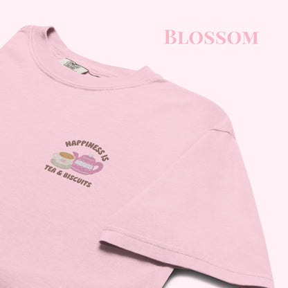 Close-up of "Happiness is Tea and Biscuits" script with a tiny embroidered teacup and teapot on a pink-coloured t-shirt