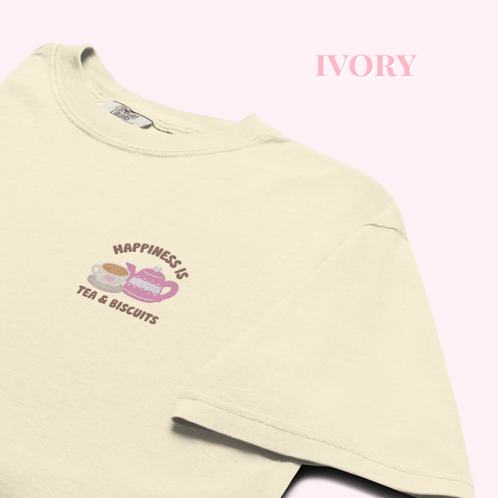 Close-up of "Happiness is Tea and Biscuits" script with a tiny embroidered teacup and teapot on a ivory-coloured t-shirt.