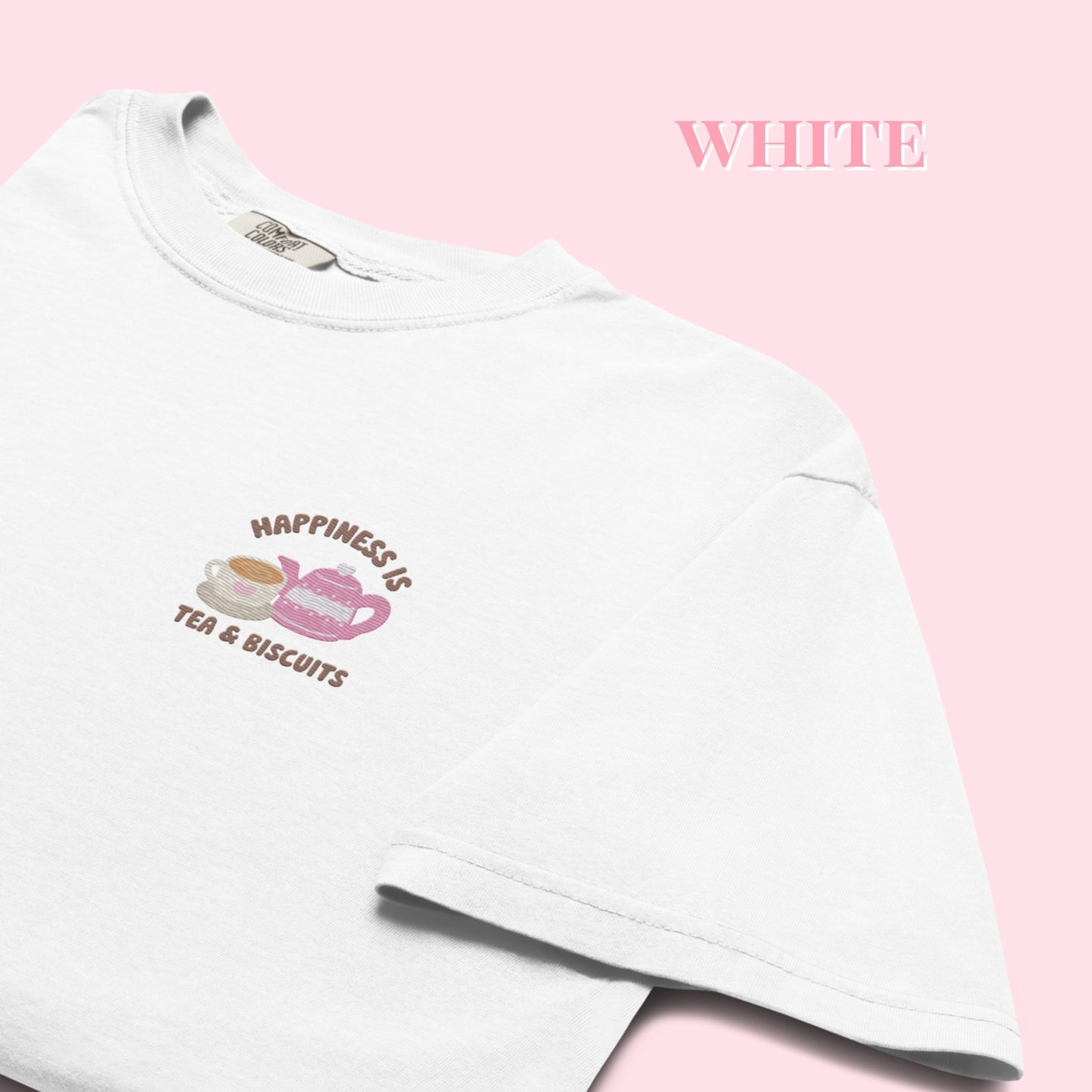 White t-shirt with a embroidered happiness is tea and biscuits design on a pink background