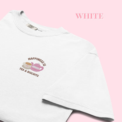 White t-shirt with a embroidered happiness is tea and biscuits design on a pink background