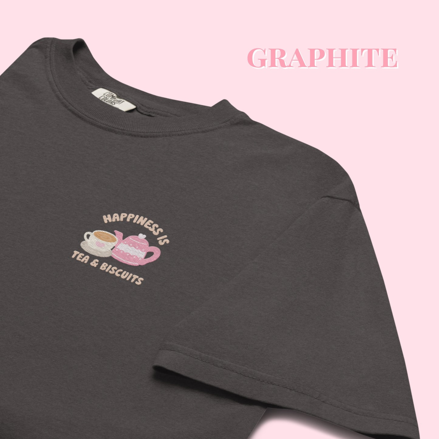 Dark gray tshirt with a embroidered happiness tea and biscuits design and text on a pink background, 