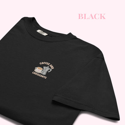 close up Embroidered black  tshirt with coffee and croissant text and a cute coffee mug and grey stove top coffee maker. slow cozy moments. coffee lover gift