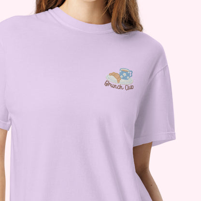 Women wearing a lilac t-shirt with 'Brunch Club' embroidered design, featuring a coffee cup and croissant illustration. Cafe slow life cozy girl