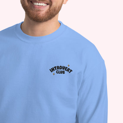 Person wearing a light blue sweatshirt with 'Introvert Club' text on a plain background