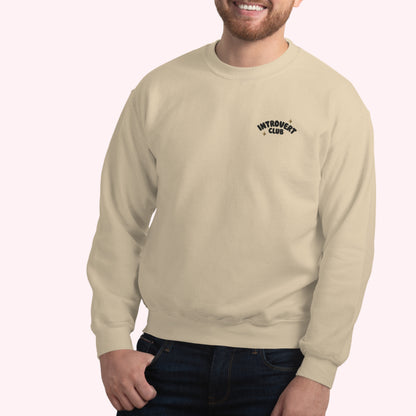 Man wearing a sand sweatshirt with 'Introverts Club' embroidered text on a white background