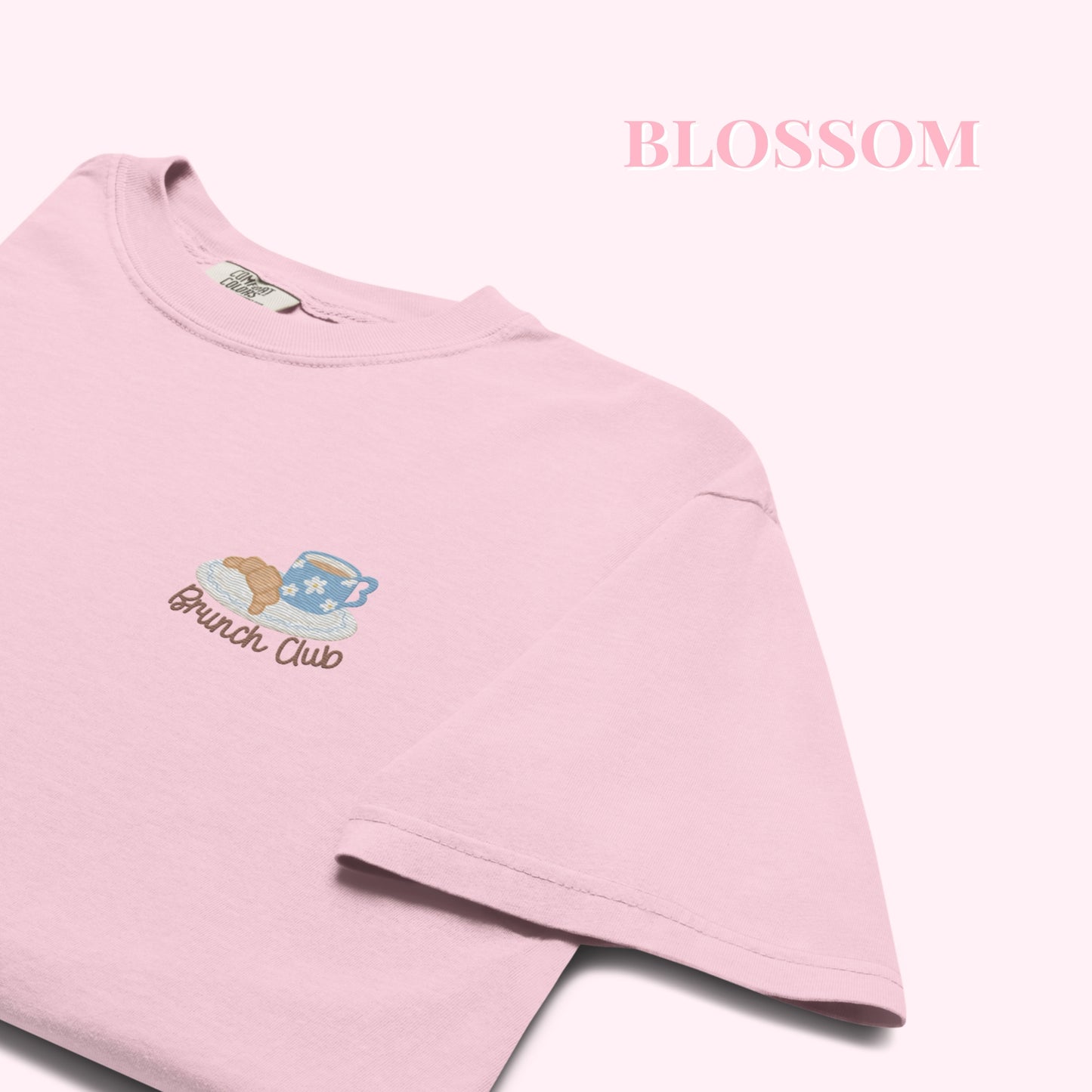 Close up of a pink t-shirt with 'Brunch Club' embroidered design, featuring a coffee cup and croissant illustration. Cafe slow life cozy girl