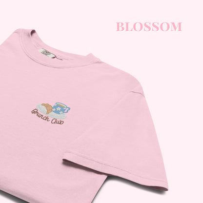 Close up of a pink t-shirt with 'Brunch Club' embroidered design, featuring a coffee cup and croissant illustration. Cafe slow life cozy girl