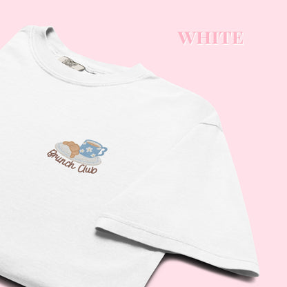 Close up of a white t-shirt with 'Brunch Club' embroidered design, featuring a coffee cup and croissant illustration. Cafe slow life cozy girl