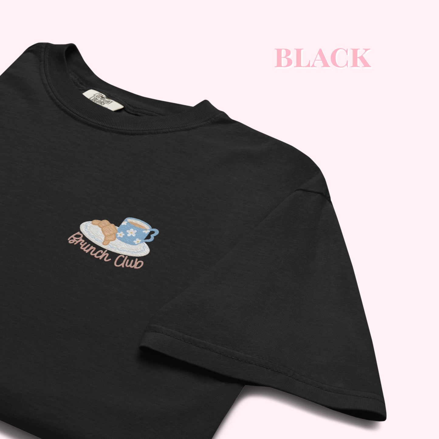 Close up of a black t-shirt with 'Brunch Club' embroidered design, featuring a coffee cup and croissant illustration. Cafe slow life cozy girl