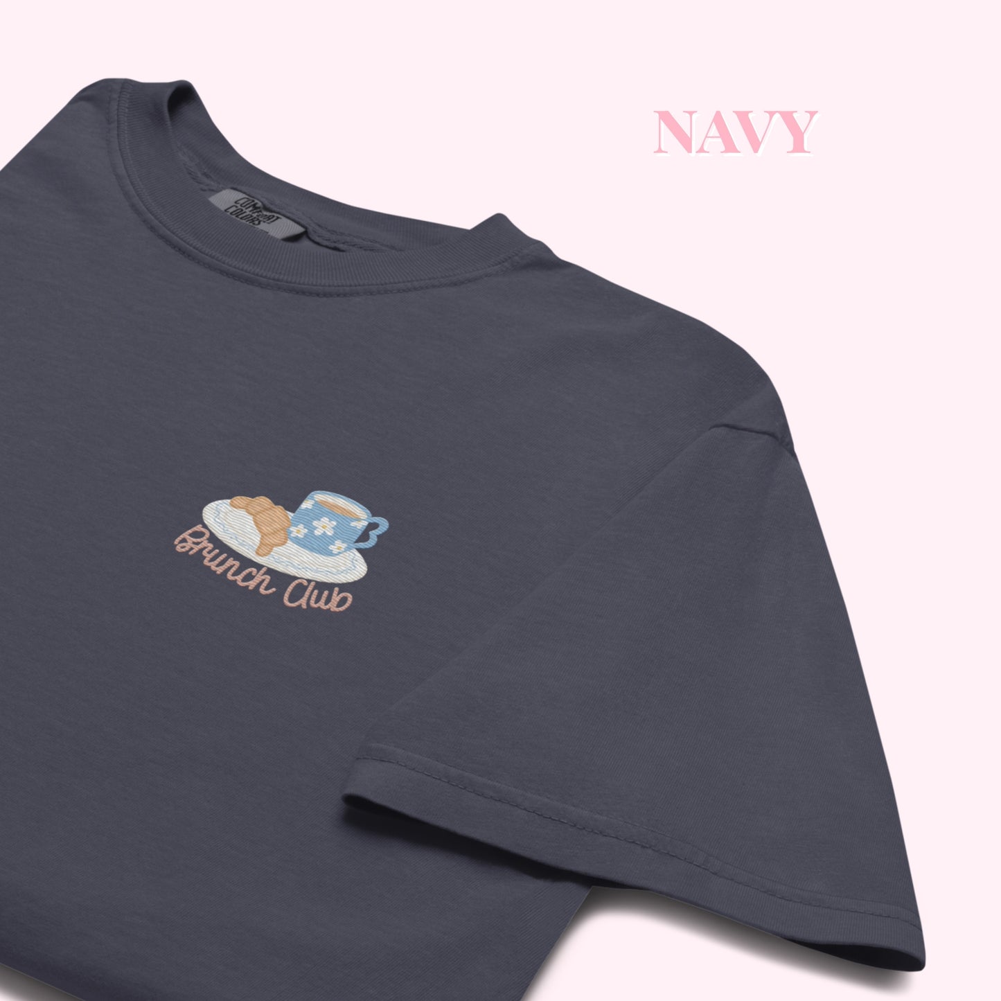 Close up of a navy t-shirt with 'Brunch Club' embroidered design, featuring a coffee cup and croissant illustration. Cafe slow life cozy girl