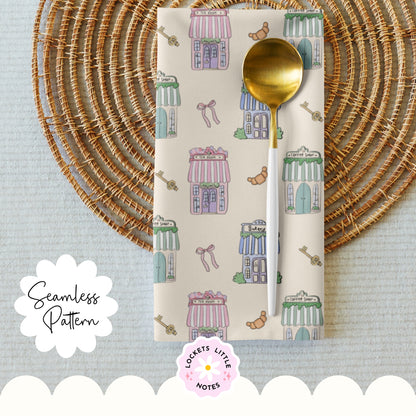 Napkin with cute pattern, gold spoon, and 'Lockets Little Notes' branding on a textured surface. Seamless pattern on a cream background featuring hand-illustrated pastel shops, including a bakery, tea house, and coffee shop.
