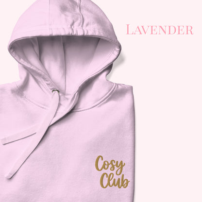 A folded lavender hoodie with a gold 'Cosy Club' script logo on the front, set against a pale pink background with the word 'LAVENDER' printed in the top right.