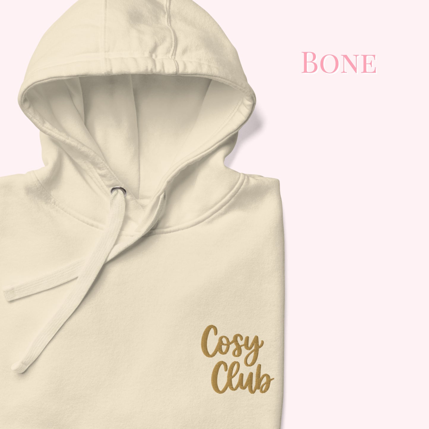 A cream-colored hoodie with a gold 'Cosy Club' logo on the chest, shown against a pale pink background with the text 'BONE' in the upper right.