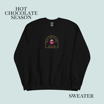 Black sweater with 'Hot Chocolate Season' logo on a light blue background