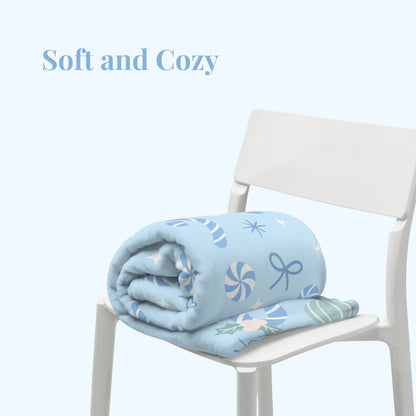 Folded blue blanket with Christmas patterns on a white chair, labeled 'Soft and Cozy'.