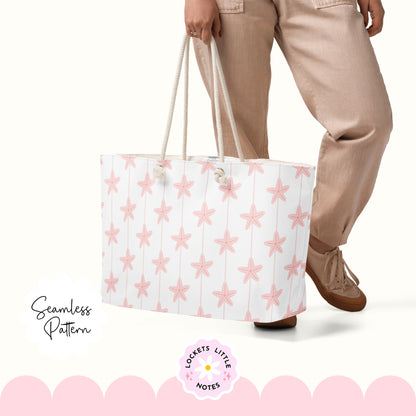 Seamless coastal pattern featuring a crisp white background with fine vertical pink pinstripes and a repeating scatter of detailed pink starfish. Person holding a white tote bag with pink star pattern, wearing beige pants and brown shoes.