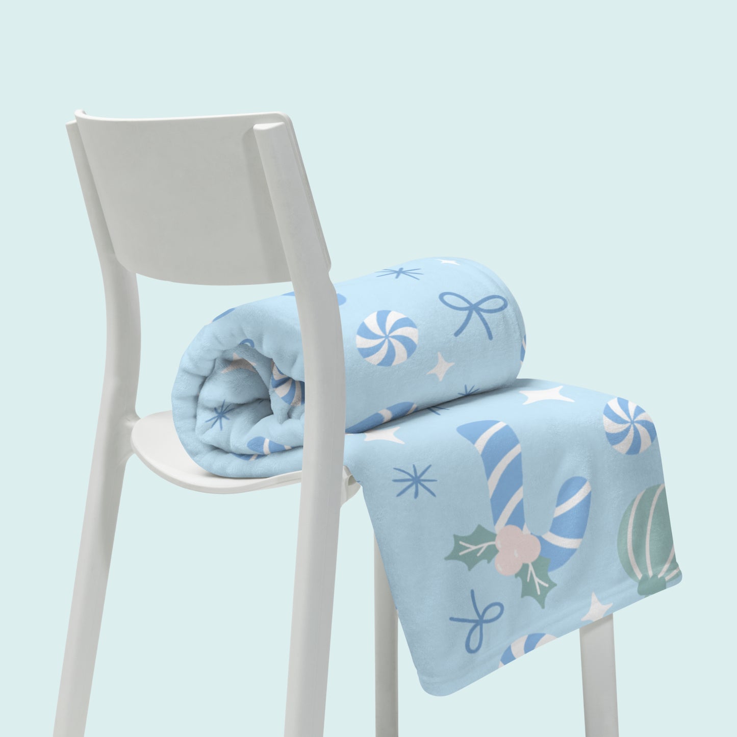 Light blue blanket with candy cane christmas themed design on a white chair against a light blue background