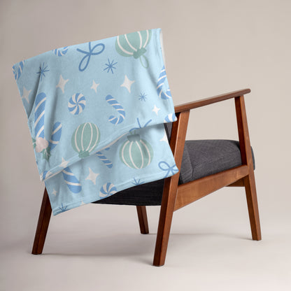 Light blue blanket with candy cane christmas pattern draped over a wooden chair.