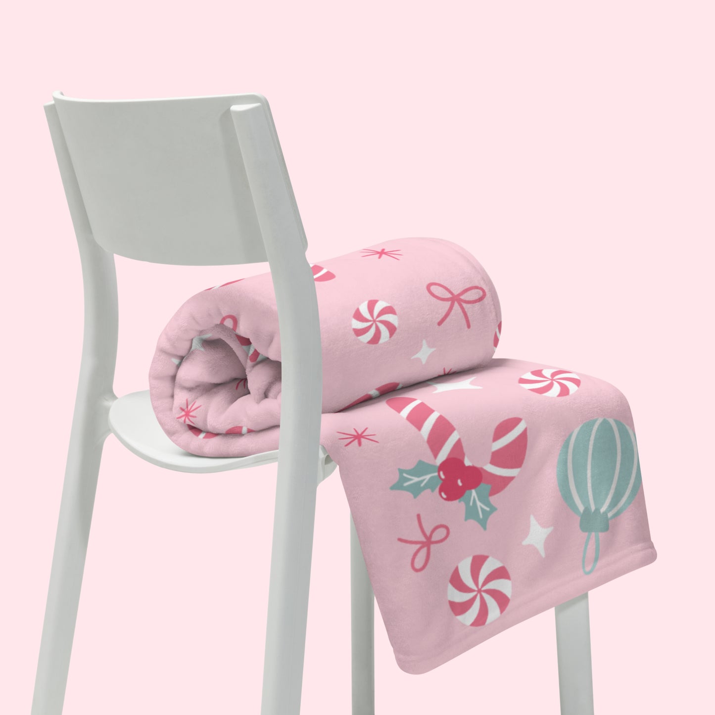 Pink christmas blanket with candy cane themed design on a white chair against a pink background