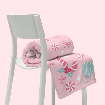 Pink christmas blanket with candy cane themed design on a white chair against a pink background
