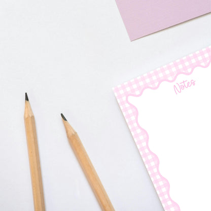 Two pencils on a white surface with a pink notebook in the background pastel gingham notepad, watercolor café illustration details, and GoodNotes iPad tablet templates.
