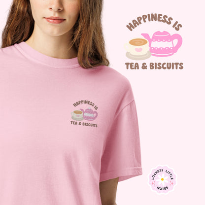 Close-up of "Happiness is Tea and Biscuits" script with a tiny embroidered teacup and teapot on a pink-coloured t-shirt worm by a women